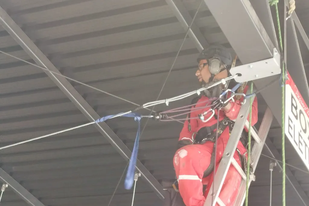 Profissional em uma escada presa a uma linha de vida instalada sob a cobertura de um galpão
