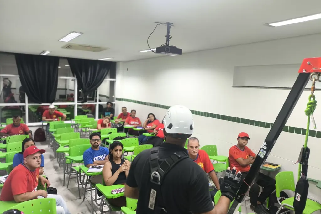 Instrutor com cinto de segurança e tripé de resgate dando aula para uma turma