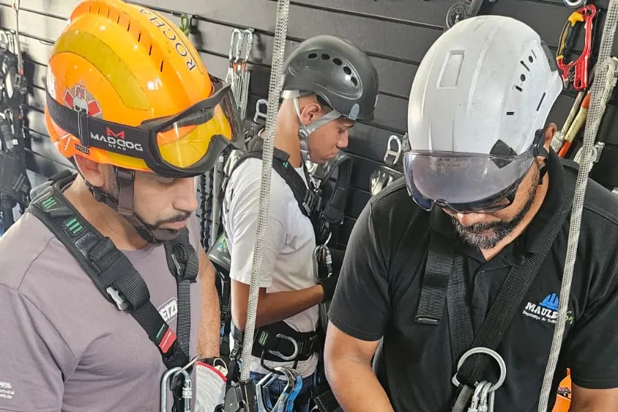Alunos de capacete ajustando cintos e cordas durante um treino prático de trabalho em altura