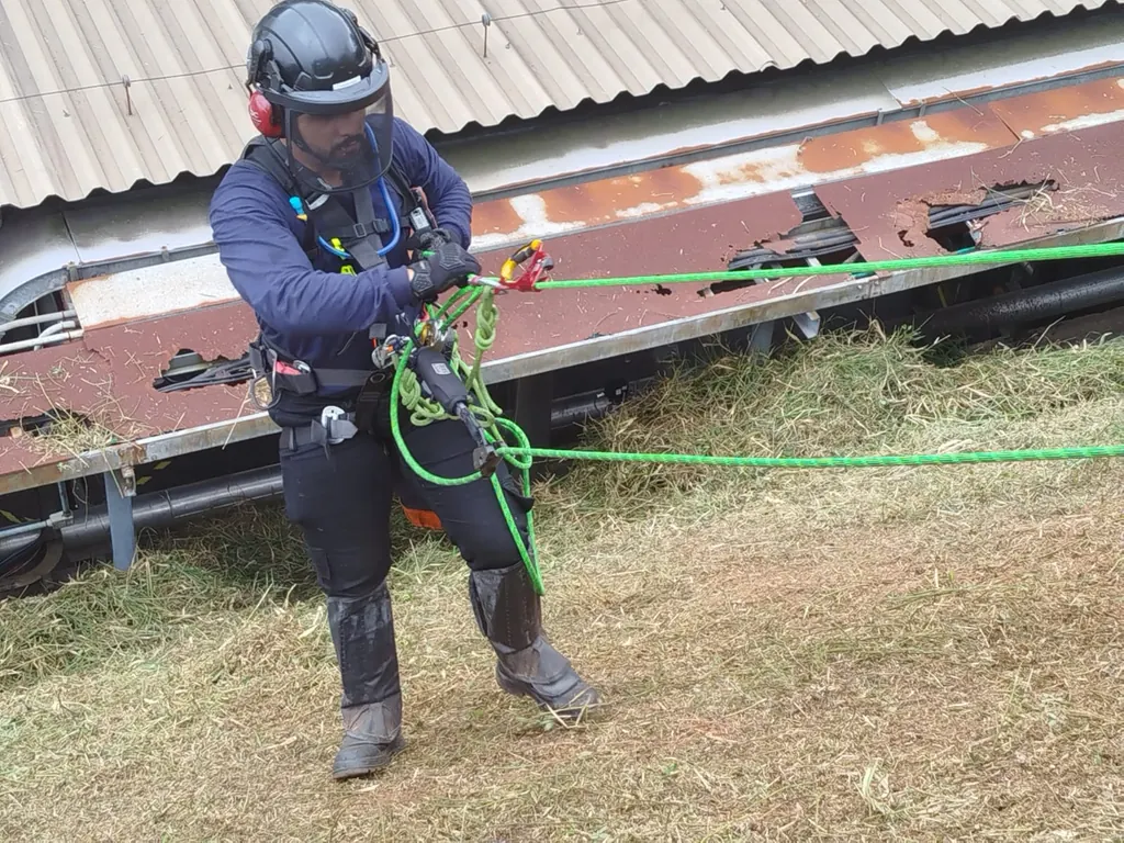 Profissional de capacete, viseira e protetor auricular operando um sistema de cordas durante um resgate ao ar livre