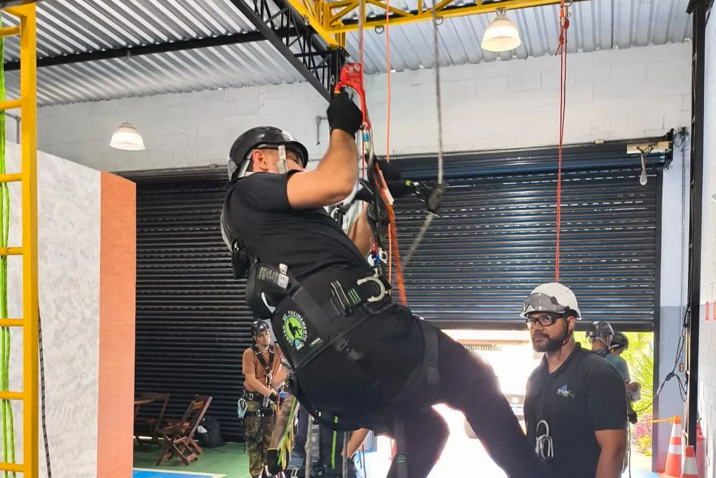 Profissional suspenso por cordas em treino de resgate, acompanhado por um instrutor