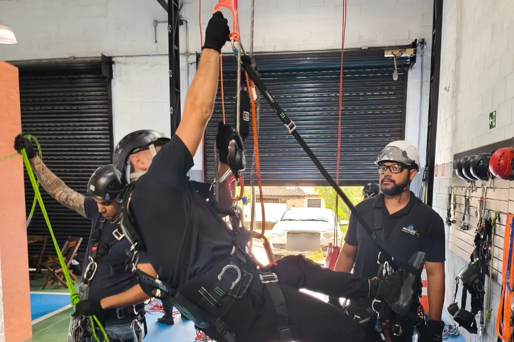 Aluno suspenso por cordas em treino de resgate técnico, acompanhado por instrutores
