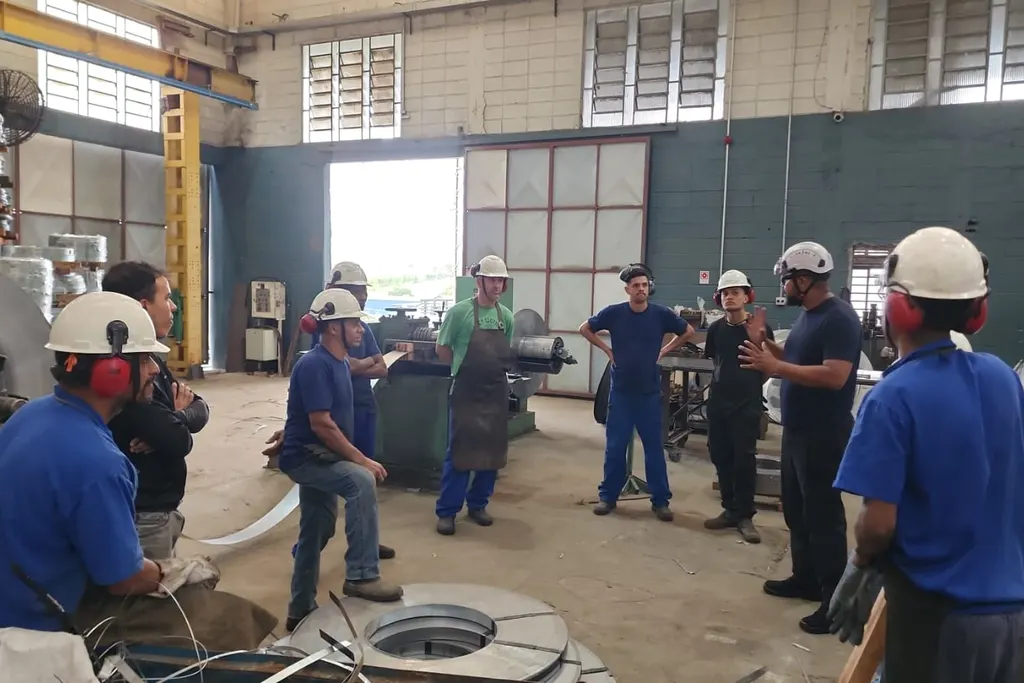 Profissional de segurança orientando um grupo de trabalhadores de capacete dentro de uma fábrica